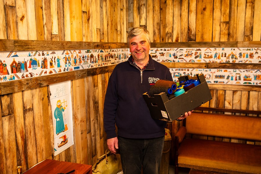 Jóhannes Eyberg Ragnarsson, formaður Eyrbyggjasögufélagsins, heldur hér á ullarband sem verður notuð til að sauma 26 metra langan refil sem myndgerir Eyrbyggjasögu. Aftan við hann má sjá refilinn í smækkaðri mynd á pappír. 